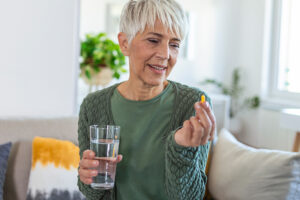 senior lady holding supplement and glass of water