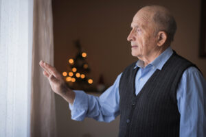  An older man shows signs of seasonal affective disorder as he solemnly looks out the window of his home.