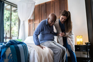 A senior receiving live-in care services gets help getting out of bed.