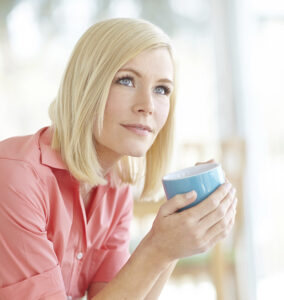 A young woman holds a coffee mug and looks off into the distance as she ponders how best to manage her multiple sclerosis diagnosis.