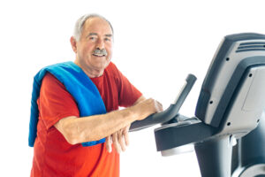 A senior man stands next to a treadmill as he contemplates the impact of exercise on Parkinson’s disease.