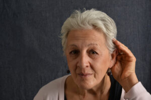 A woman with hearing loss cups her hand behind her ear to try to make out what people are saying in a group conversation.