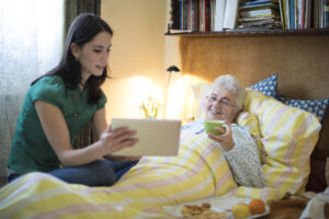 A caregiver shows her laptop to an older woman receiving post-operative care.