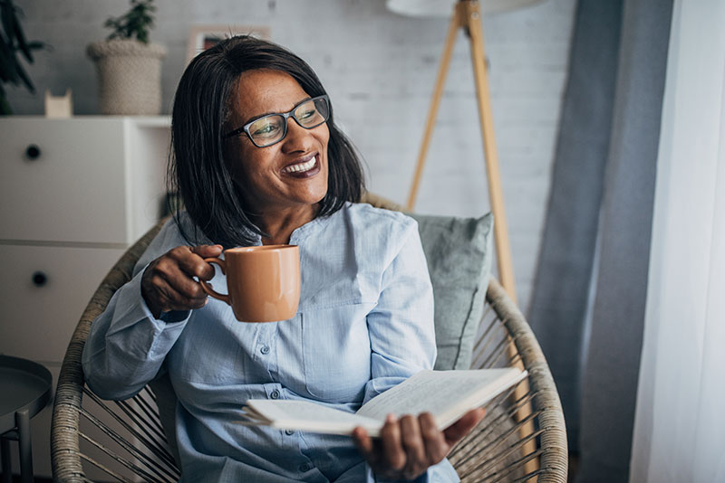 A woman enjoys reading a book while sipping a cup of tea, making time for caregiver stress relief activities.