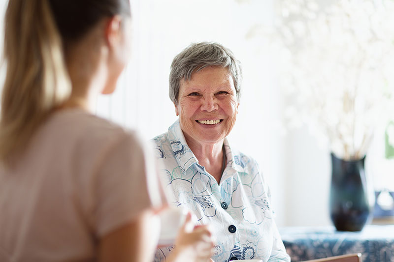 A woman diagnosed with both dementia and heart disease smiles as her caregiver helps her.