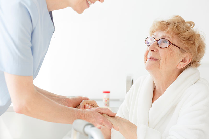 A woman receives a helping hand from her caregiver after a hospital stay.
