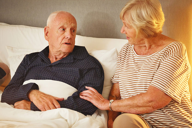 A woman helps her husband get settled into bed the first evening after surgery.